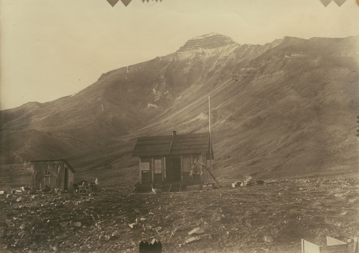 Fotografi från expedition till Spetsbergen 1920. Motiv av liten trästuga nedanför berg.