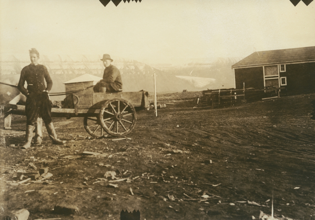 Fotografi från expedition till Spetsbergen 1920. Motiv av två män vid en träkärra framför ett hus.