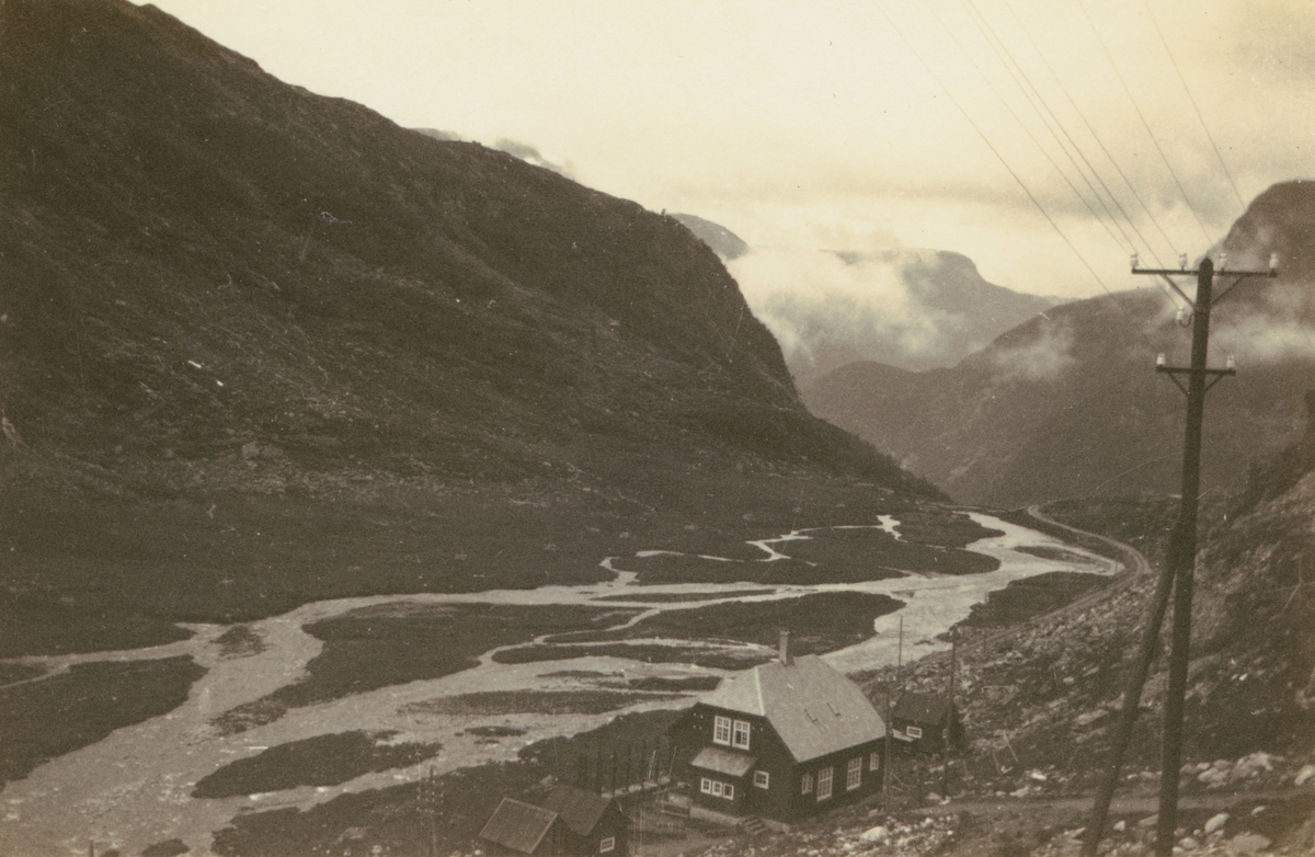 Fotografi från Albin Ahrenbergs resa till Grönland 1929. Vy över kargt bergslandskap. I förgrunden syns ett hus och telefonstolpe.