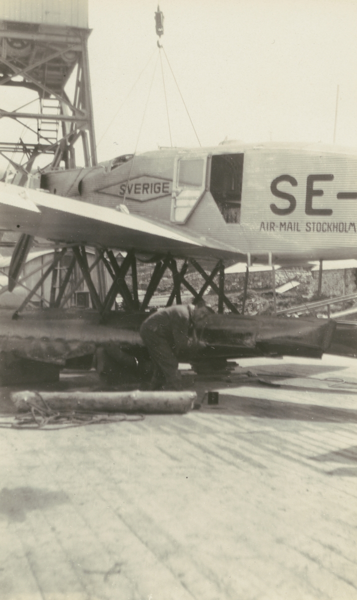 Fotografi från Albin Ahrenbergs resa till Grönland 1929. Motiv av mekaniker som arbetar på flygplan med texten: "Sverige Air-Mail Stockholm".