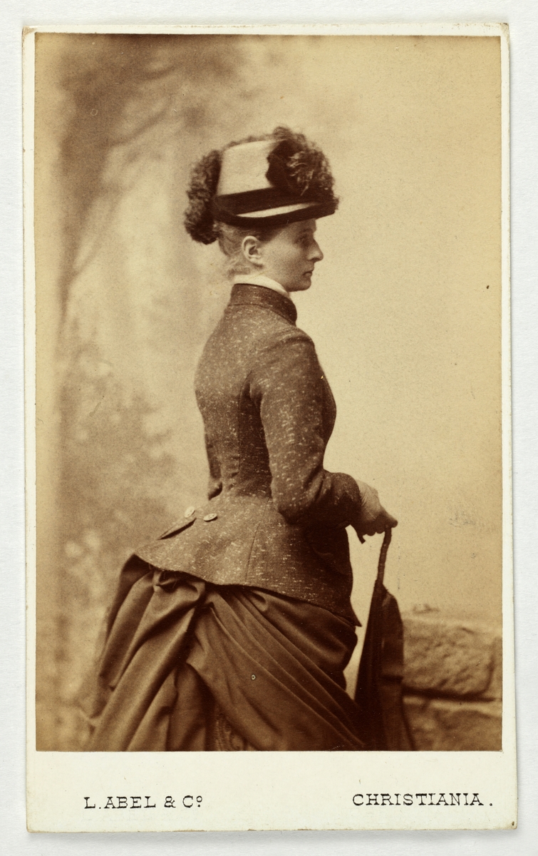 En kvinne med hatt og paraply fotografert i studio. Visittkortbilde for fru Ragnhild Heiberg, f. Meyer.