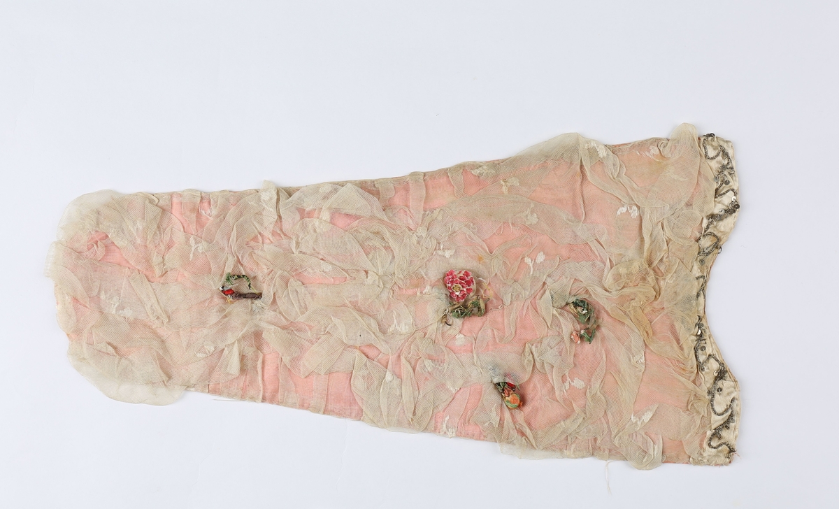 Av rosa taft, overtrukket med hvit nettedug som er lagt i folder langs begge sider og rynket som en fichu på midten. Nettedugen er ivevd små hvite silkeblomster. Ved den avrundete overkant er påsydd et stykke hvit atlask-silkebånd med bord av sølvsnor og paljetter. Nedover brystduken er påsatt små kvaster av blomster og frukter i forskjellige materiale (defekte), en rose gjenstår med blad av perlemor på papp og farget røde. Brystduken er rundet nederst og fôret med hvitt linstoff.