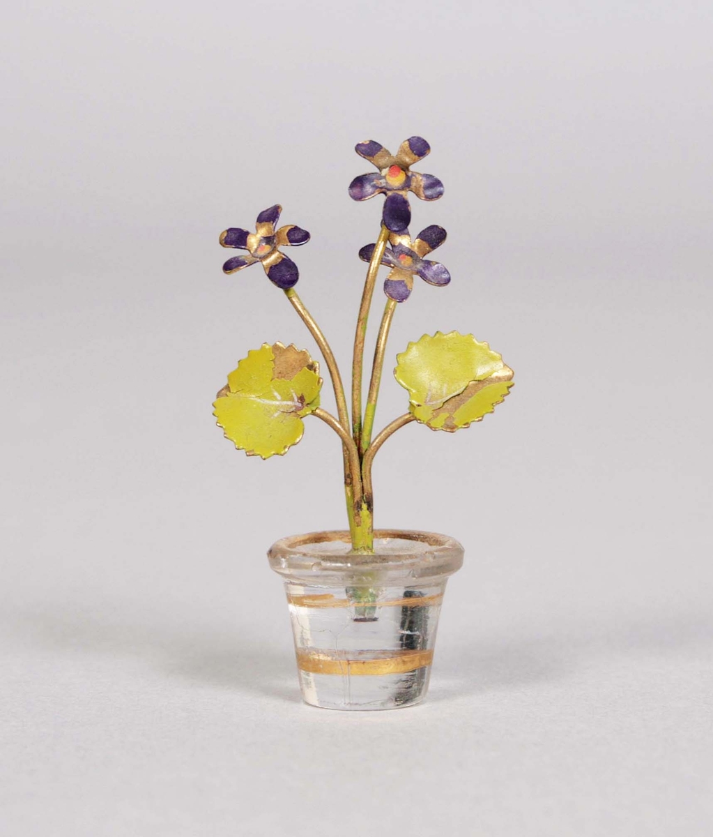 Rund kruka av glas med dekor av 2 förgyllda linjer, samt uppbärande stjälk i mässing, med 3 lilafärgade blommor och två gröna blad.