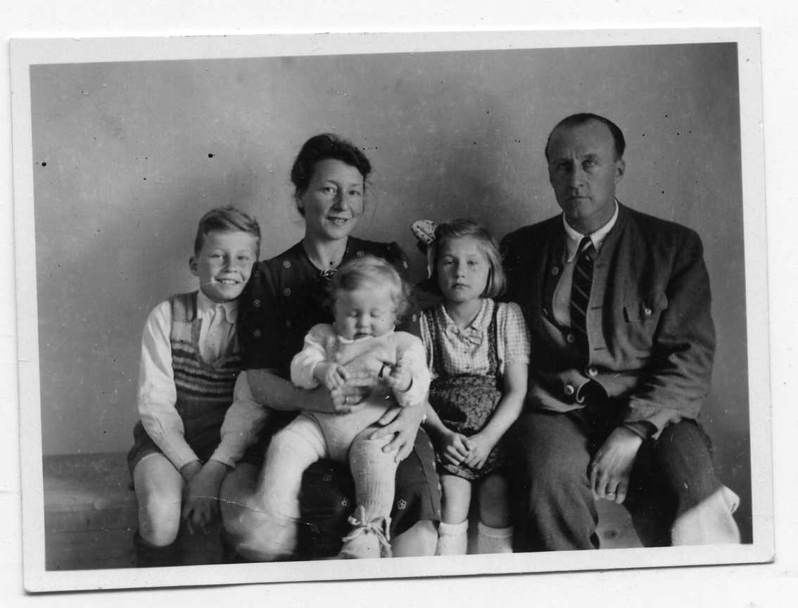 En familjegrupp: mamma, pappa och tre barn som sitter på en bänk.