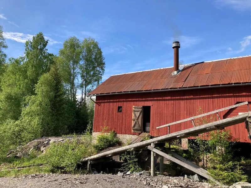 Bildet av Gaustadsjødaga. Eksteriør. Saga er rød, og rundt den er det skog og et vann.