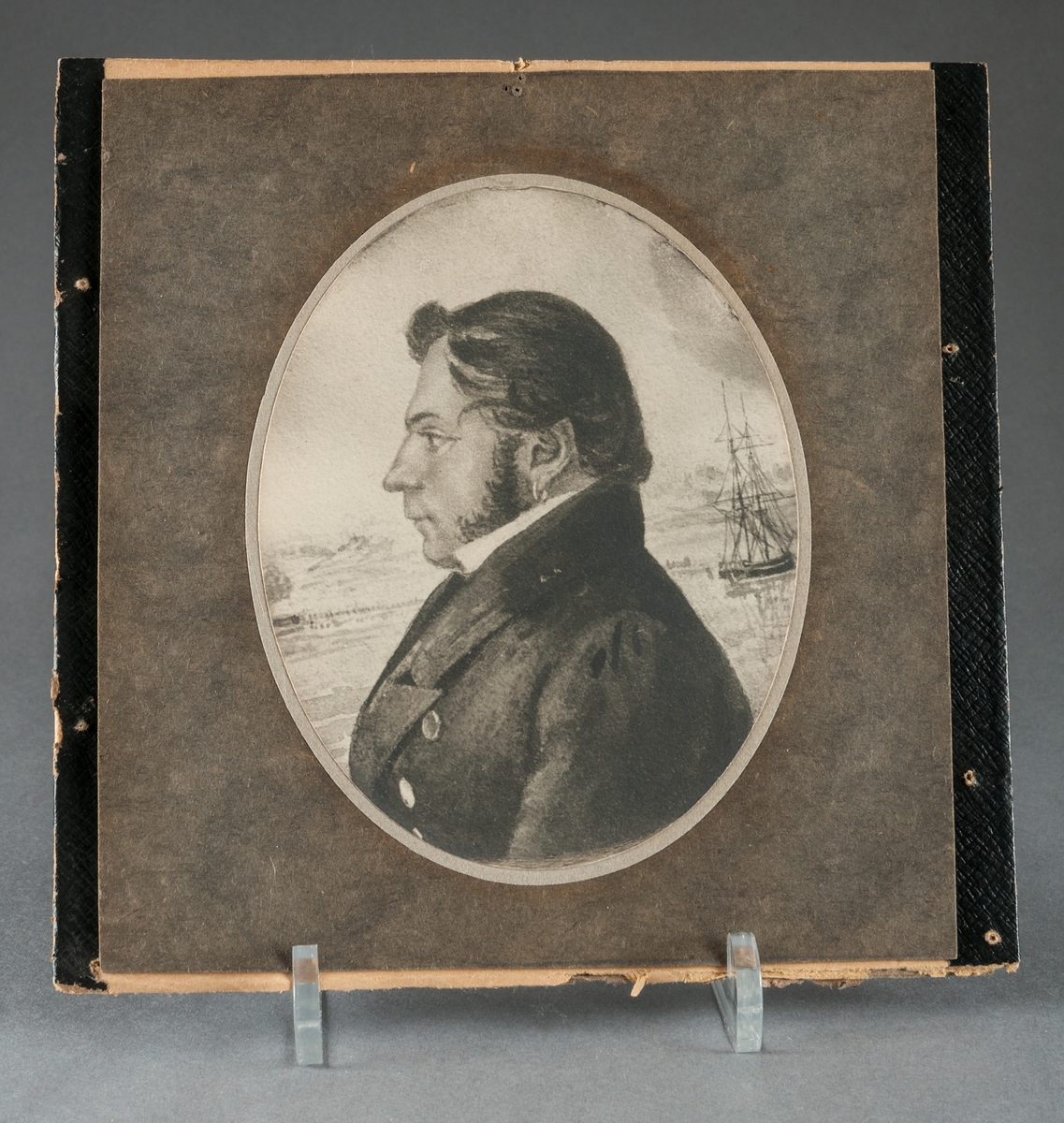 Mansporträtt i profil, grvyr. Till höger om axeln ett tvåmastat skepp. Ovalt porträtt i rektangulär svart ram. 
Porträtt föreställande Sjökapten C. J. Bolin.
