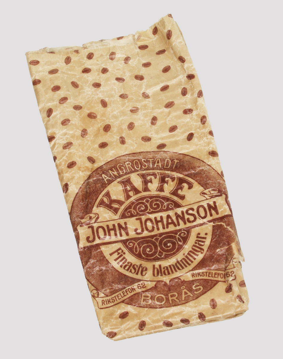 Kaffepåse i beigebrunt glansigt papper, med strödd dekor av bruna kaffebönor. Märkt: "JOHN JOHANSON, BORÅS, ÅNGROSTADT KAFFE, FINASTE BLANDNINGAR, RIKSTELEFON 62".
