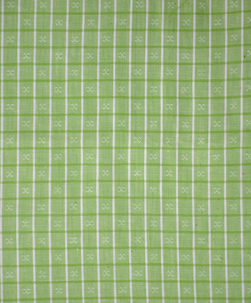 Bomullstyg, 1940-tal.
Klänningstyg med genomvävt mönster. Grön- och vitrutigt med tuskaft i botten och figurer av flotterande trådar i varannan ruta.
Varp: grönt-vitt otvinnat garn
Väft: vitt-grönt otvinnat garn