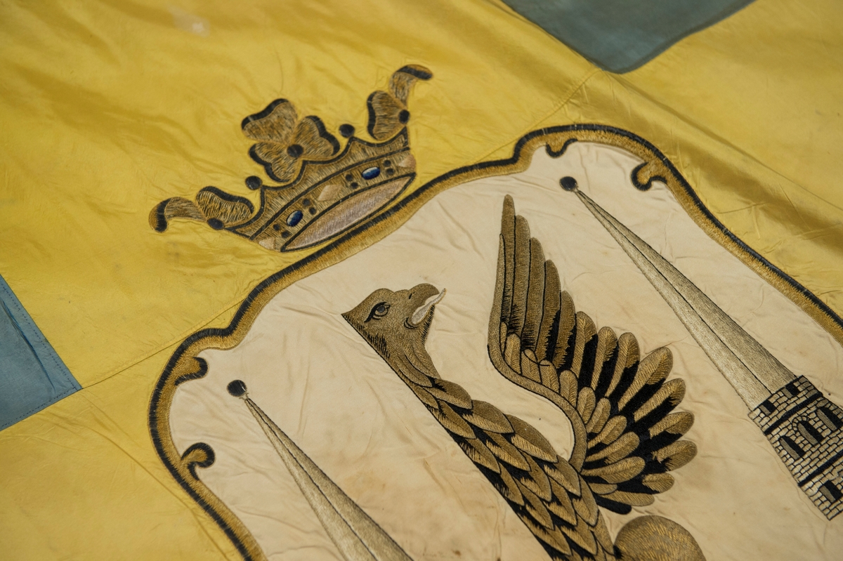 Fana av gult och blått natursiden, dubbet tyg, med heraldiskt motiv: Karlstads stadsvapen. Motivet är placerat i mitten av det gula korset och består av en applikation av vitt siden med heltäckande broderi. Fanan är fäst på vitmålad stång med en fanspets i metall med Carl XV's namnskiffer. Runt skiffret en lyrformad lagerkrans, krönt med symbolen för det allseende ögat med strålar runt.