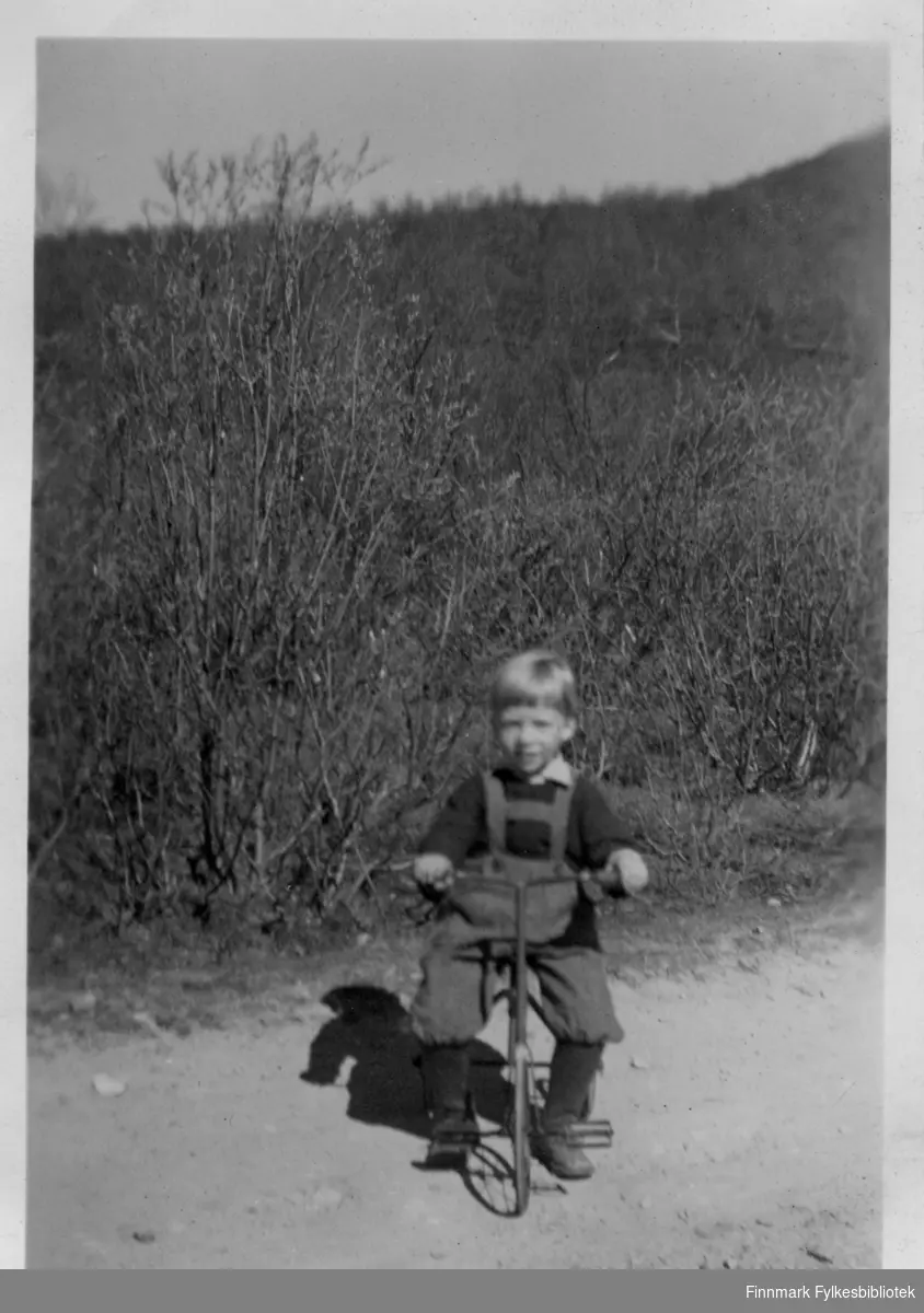 Edmund Johansen på 3-hjulssykkel, ca. 3-4 år gammel, hjemmesydd knickers med seler. Sykkelen har Edmund fortsatt. Bildet er tatt på hjemmegården i Kunes rundt 1949-1950.