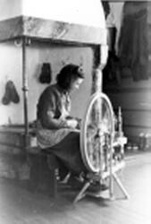 Maline Klepp (f. Dagsgard 1929) sit og spinn ved peisen i ne