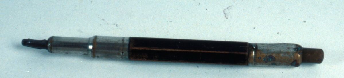 Ritpenna med svartmålad trästomme och metallhylsa, vari ett kraftigt bly skjuts in.