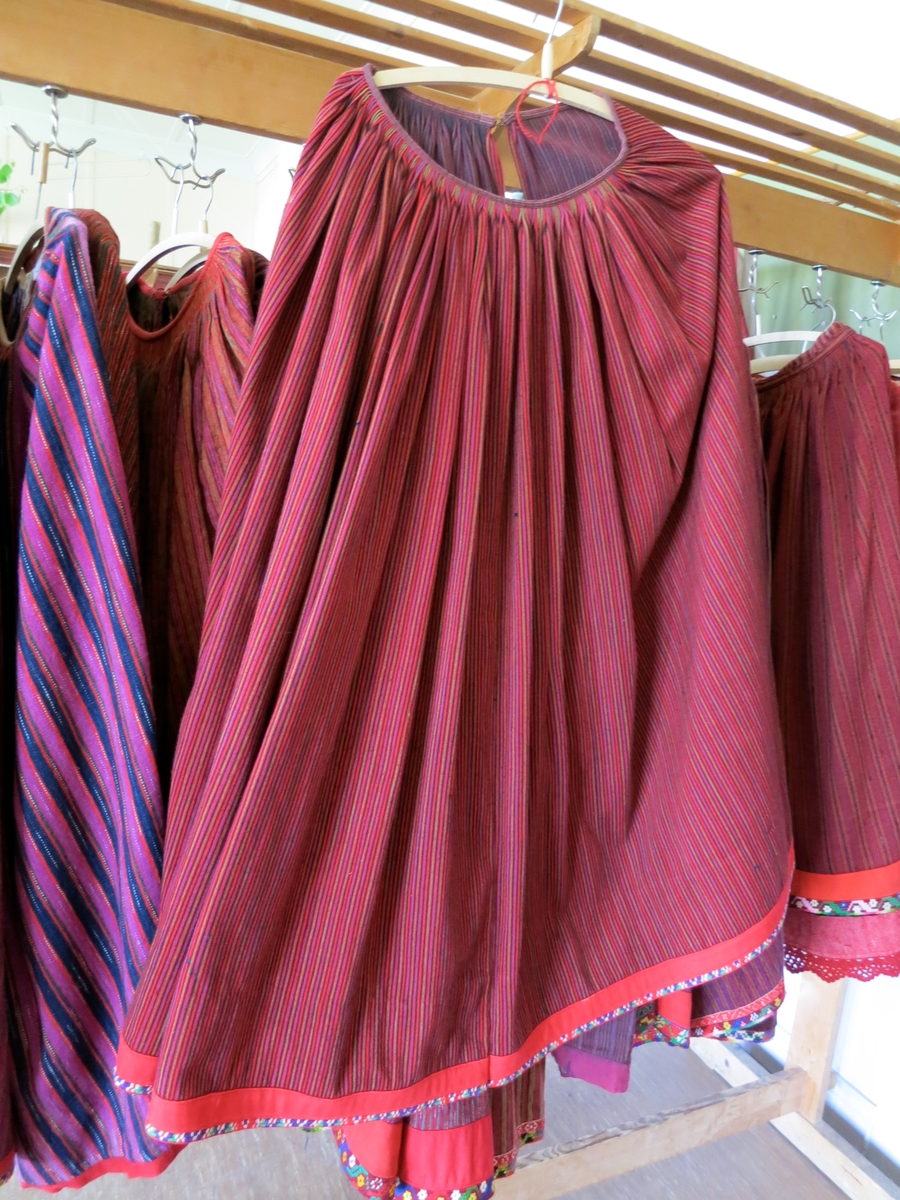 Kjol i halvylle med smala ränder i rött, svart, grönt och lila. Inget fläckgarn. Nertill skodd med smal klädeskant och smal flerfärgsvirkad flätta (2 varv).