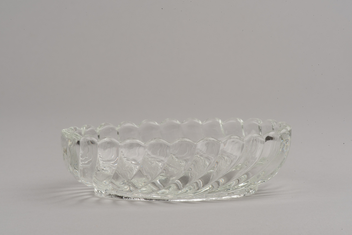 Oval skål av ofärgat glas. Pressad yttäckande dekor i form av spiralvridna åsar som avslutas i en vågformig kant.