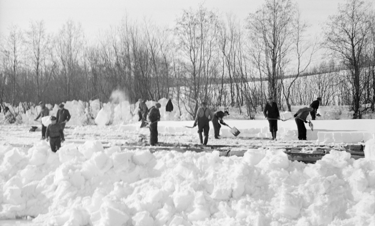 Snørydding ved lenseanlegget på Fetsund i Akershus vinteren 1941. Fotografiet viser cirka 10 menn som måkte snø fra isen med spader, antakelig for å fristille jernpongtonger som lå i isskorpa.