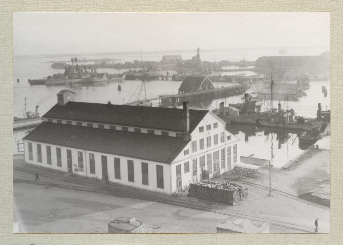 Bilden föreställer en vy ur Mönstersalbyggnader över Karlskronavarvet. I förgrunden syns Tackelkammaren och bakom den den gamle kranboden som brann ner 1969.