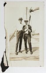 To unge menn står på en trelast med et skip i bakgrunnen, an