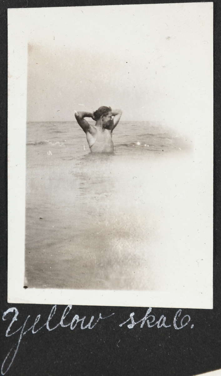 Mann med armene løftet i positur, står med vann til midjen i havet.
