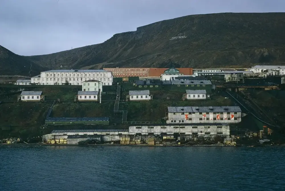 Bilde av Barentsburg, tatt fra Grønnfjorden. Havneannlegg med bebyggelse og fjell bak.