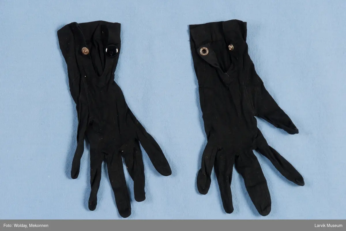 Et par sorte hansker med stikninger og sort trykkknapp