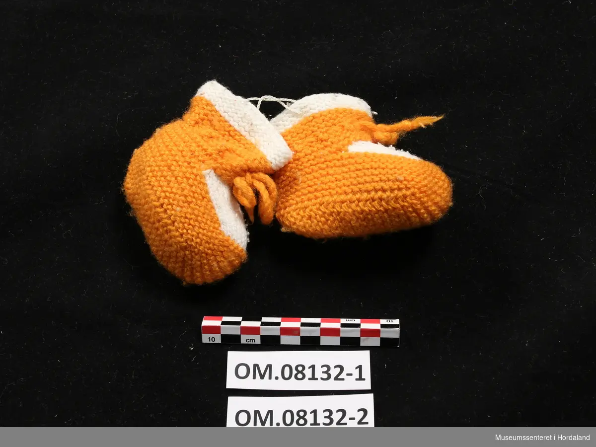 Sokkepar til baby strikket av garn i oransje og hvitt ull.