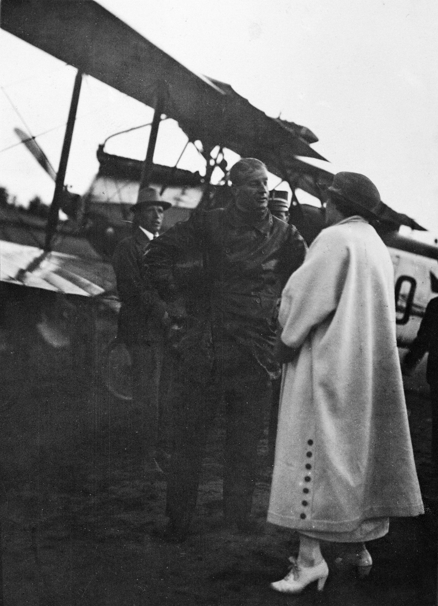 En kvinna pratar med en flygare framför flygplan FVM S 18, omkring 1920-1926. Två män i bakgrunden.