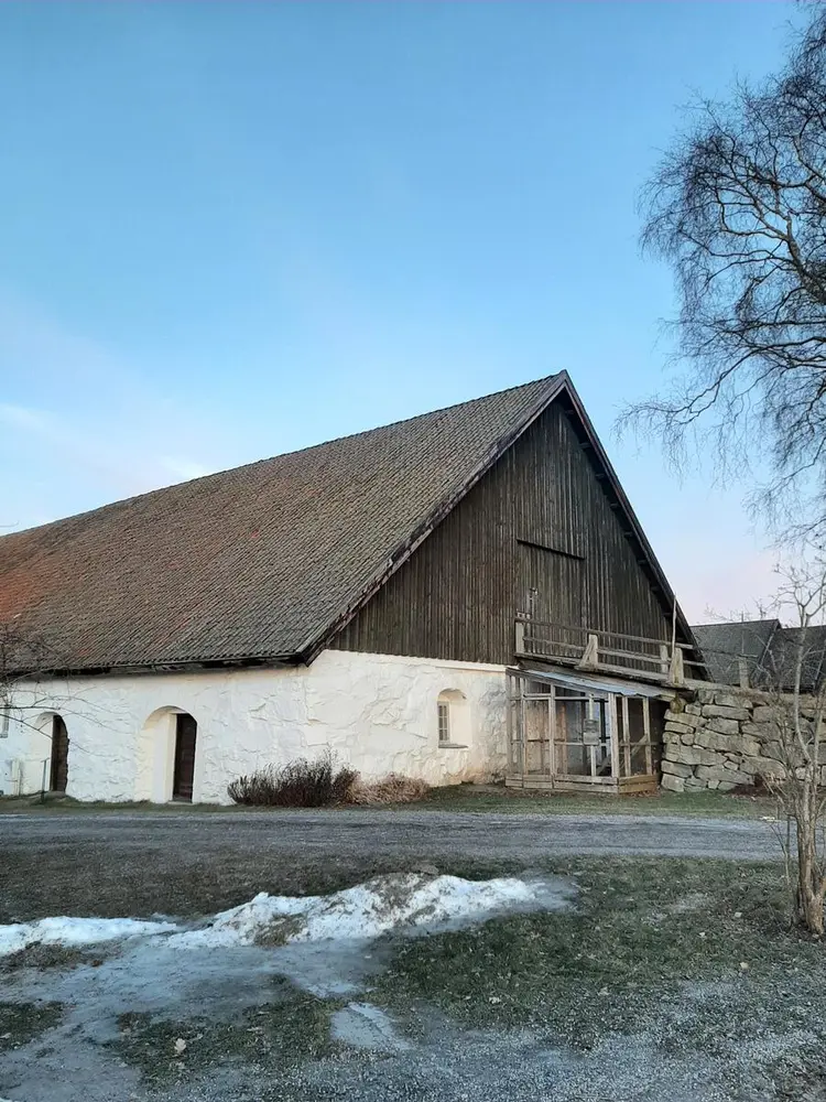 Bildet viser fremsiden av det hvitt steinfjøs. Fjøset er delt i to, der det er hvitt på undersiden og brun plank på oversiden av det hvite.