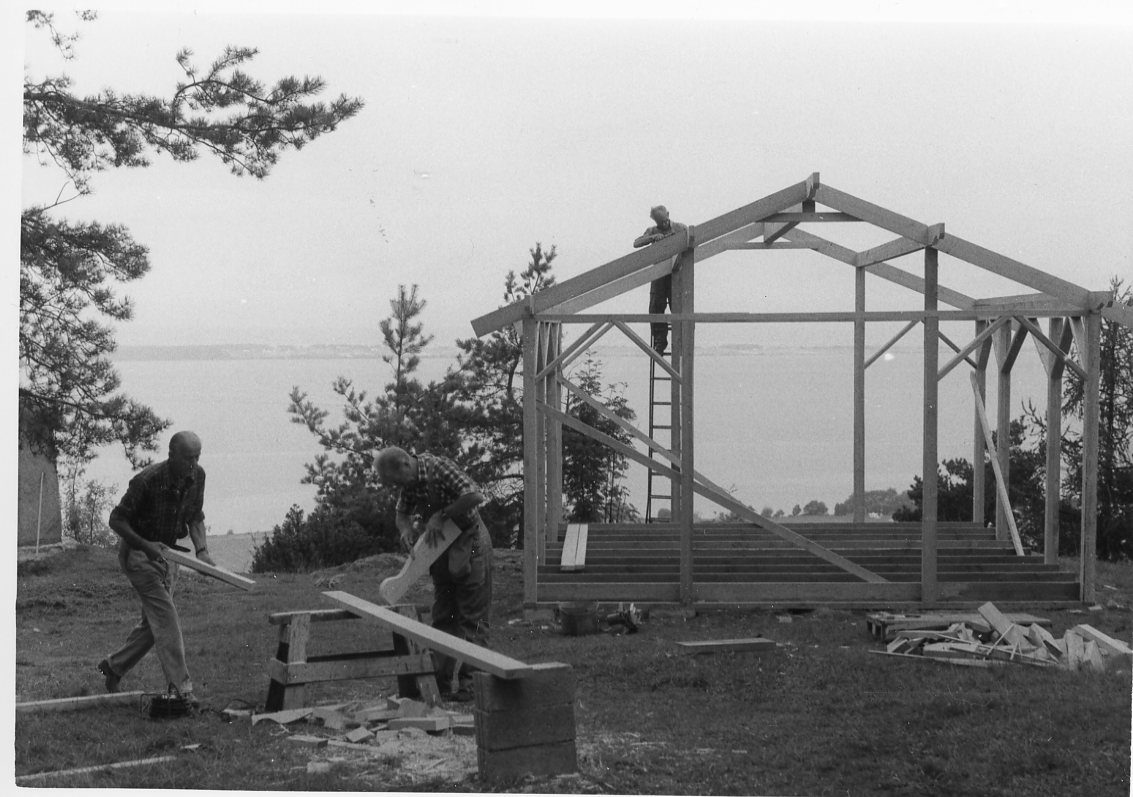Byggnadsarbete på en paviljong på Grännaberget. En man står på en stege vid västra gaveln, två män arbetar med virke.