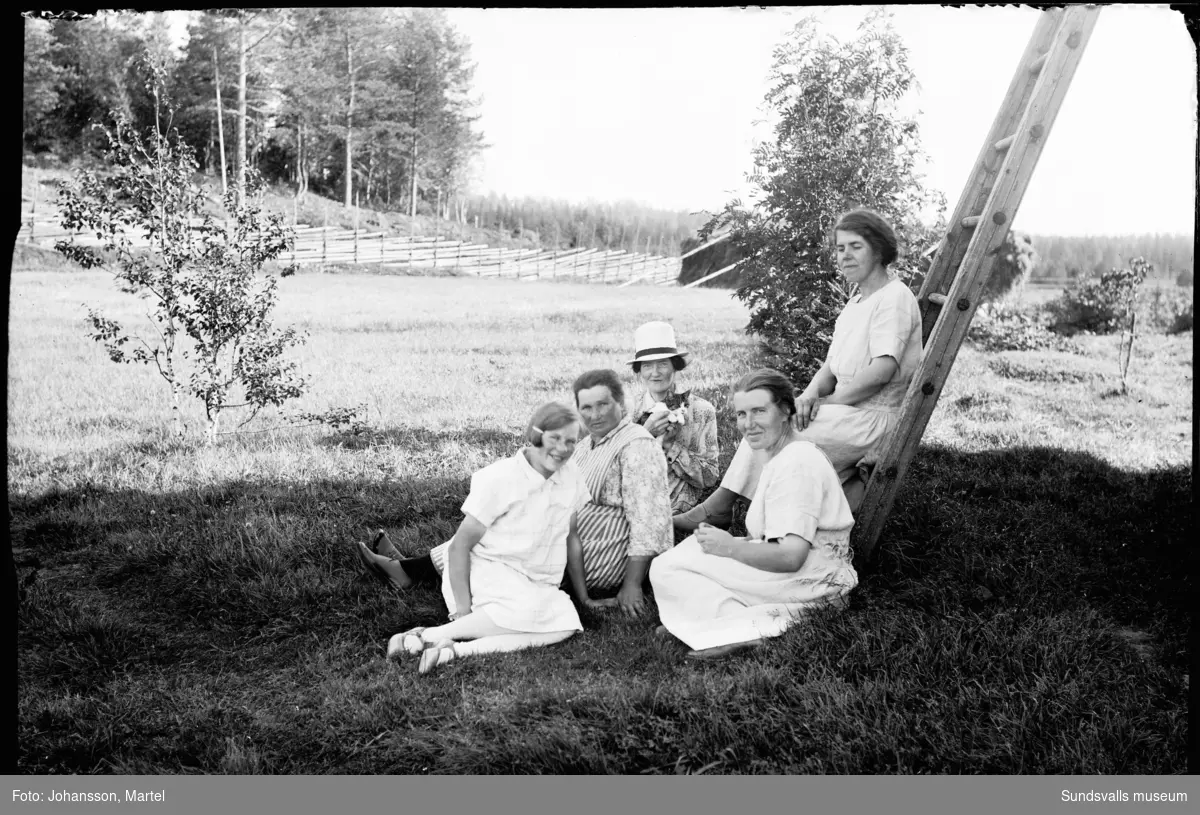 Gruppbild med fem kvinnor på gården Brännsvedjan i Sörfors. På stegen sitter Johanna "Hanna" Johansson och framför hennes syster Märta Johansson. Kvinnan med hatt är Althea Söderström, lärarinna från Indal. Övriga är oidentifierade.