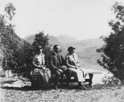 Tre personer som sitter på en benk på et utsiktspunkt med et