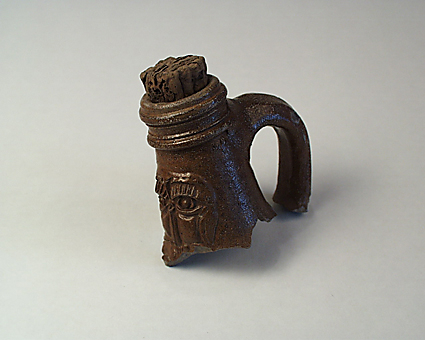 Keramik, hals och hänkel till Bartmannkrus, stengods. Kork sitter kvar i halsen. Övre delen av ett mansansikte; ögon, ögonbryn och näsa.