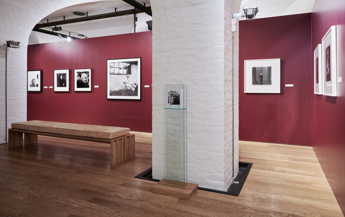 Bildet viser en av utstillingsrommene med røde vegger og fotografier tatt av Morten Krogvold hengende på rad og rekke.