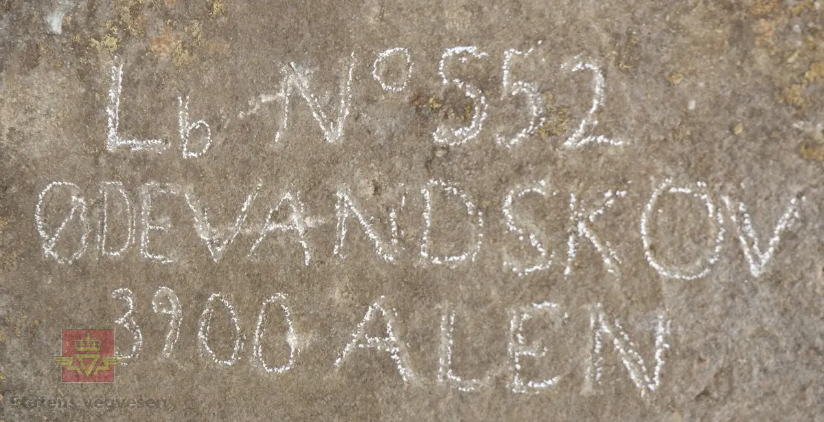 Grovt tilvirket stein med inskripsjon i øvre del. 
Steinen er merket: "Lb No552, ØDEVANDSKOV, 3200 ALEN"