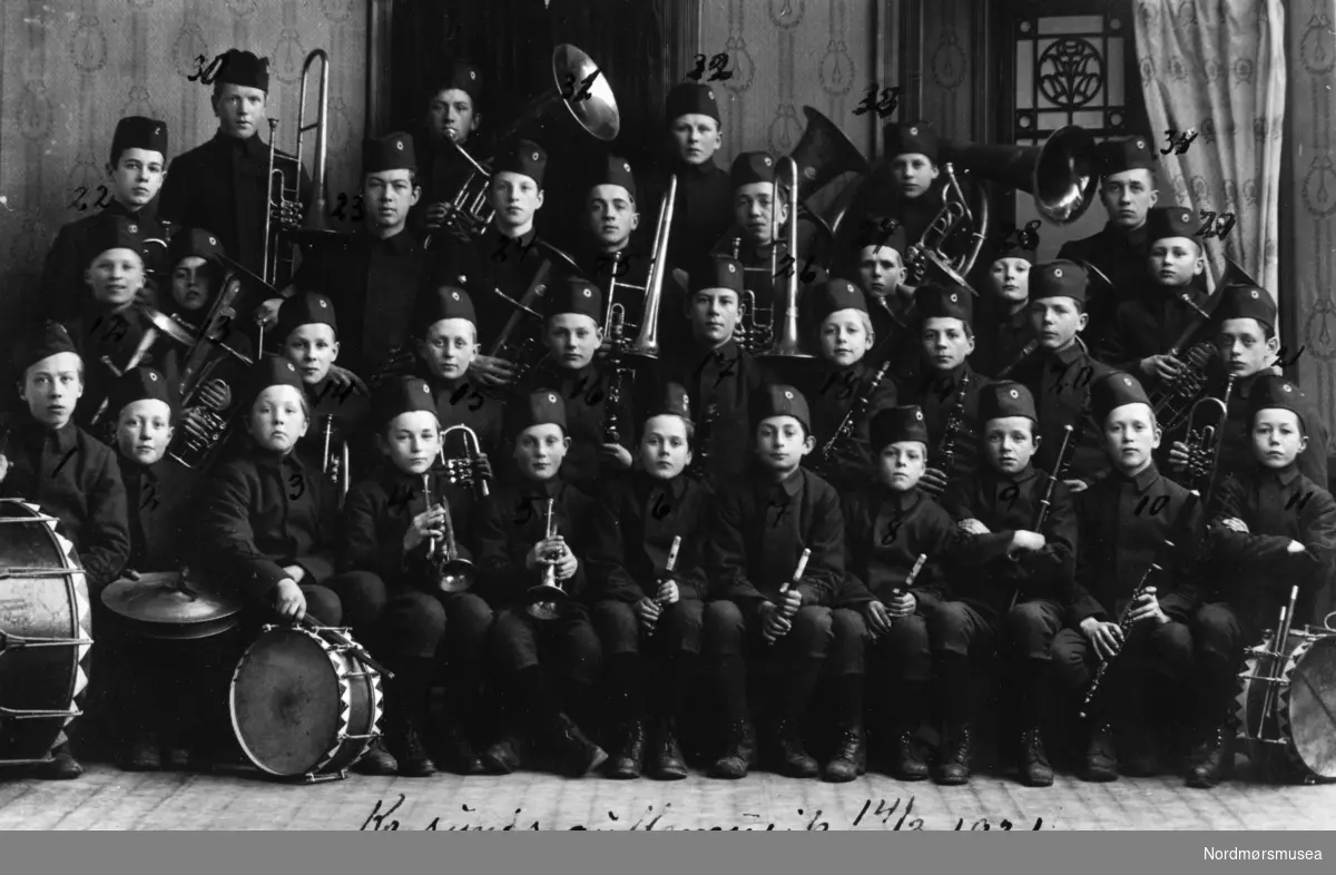 Kristiansunds guttemusikkorps 14. mars 1921. Fotograf er Ole Egge. På bildet ser vi: 1. Johan Pettersen, 2. Petter Olsen, 3. Marin Løvaas, 4. Sverre Heggem, 5. Haakon Angvik, 6. Karl Brantzæg, 7. Karl Erlandsen, 8. Karl Torkildsen, 9. Øivind Larsen, 10. Nils Heyerdahl, 11 Herlof Harstad, 12. Reidar Larsen, 13. Paul Halaas, 14. Johan Røe, 15. Sverre Olsen, 16. Ragnar Hagen, 17. Hans Larsen, 18. Edv. Ringkjøp, 19. Johan Sivertsen, 20. Artur Nilsen, 21. Odd Egge, 22. Sverre Tørlen, 23. Ole Knudset, 24. Dagfin Schau, 25. Nidolf Haugan, 26. Knut Harstad, 27. Erling Halten, 28. Odd Gaupseth, 29. Karsten Sunde, 30. Olaf Halten, 31. Harald Haln, 32. Birger Hodne, 33. Hans Olsen og 34. Hans Harstad. Fotografier fra protokollen til Kristiansunds Guttemusikkorps i perioden 1917-1927. Protokollførere var brødrene Hans og Herlof Harstad. Protokollen er i museets privatarkiv under nr. 684. Giver av protokollen er Knut Harstad. Fra Nordmørsmusea sin fotosamling.
