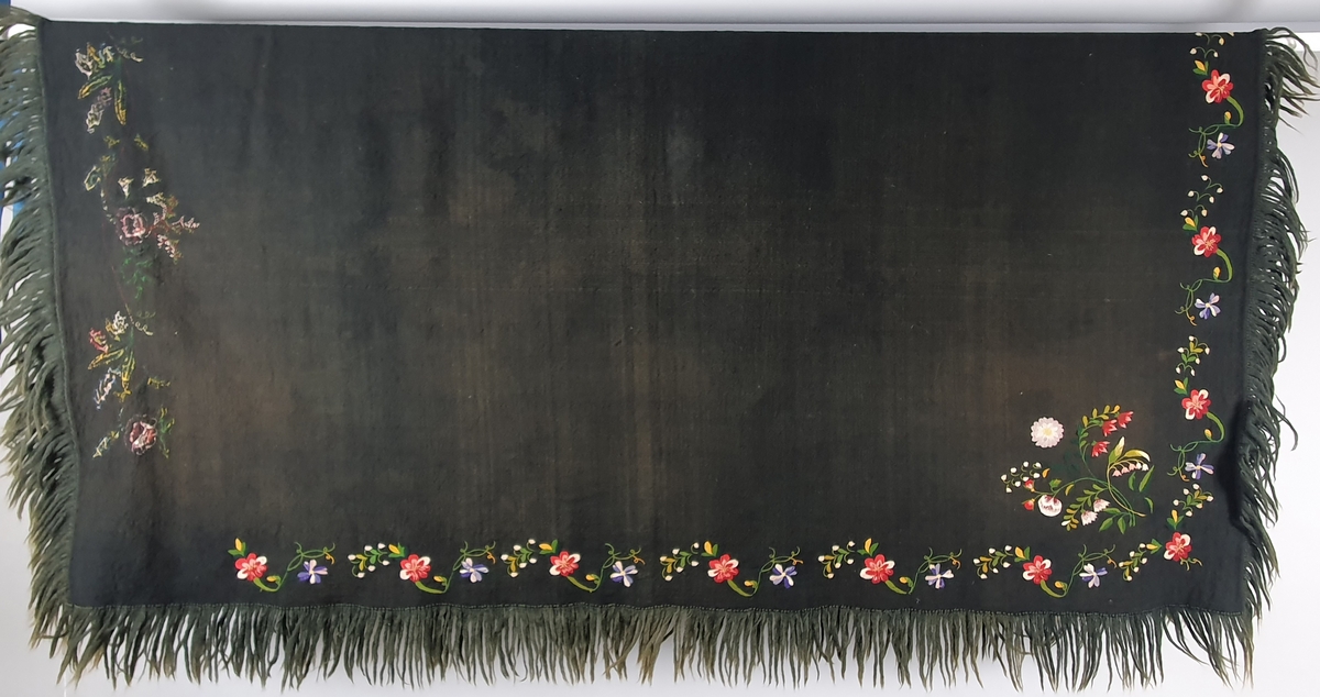 Hjemmevevd, svart bunadssjal med blomsterbroderier og frynser. Sjalet er sydd sammen av to med søm på midten. Det ene blomstermotivet er brodert på baksiden, slik at når sjalet er brettet diagonalt, er begge broderiene på yttersiden.