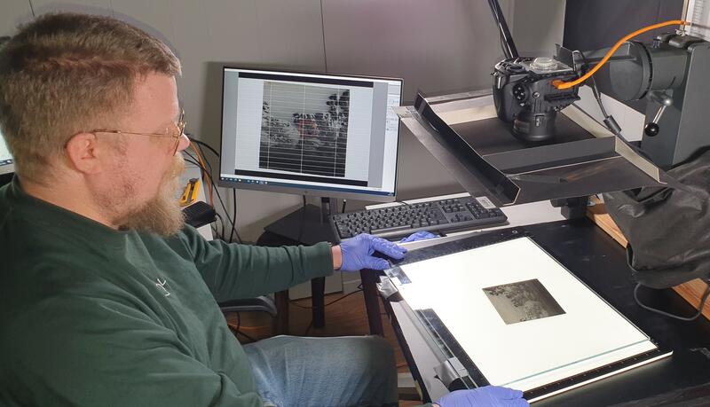 Mann som sitter ved en pult med teknisk utstyr for digitalisering av gamle foto.