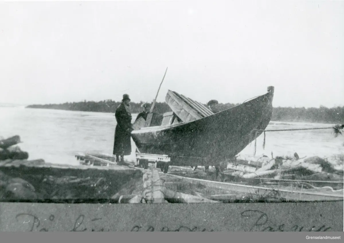 Noen personer med en båt på tur oppover Pasvik. De tar i bruk trallebanen (muligens ved Melkefoss). 