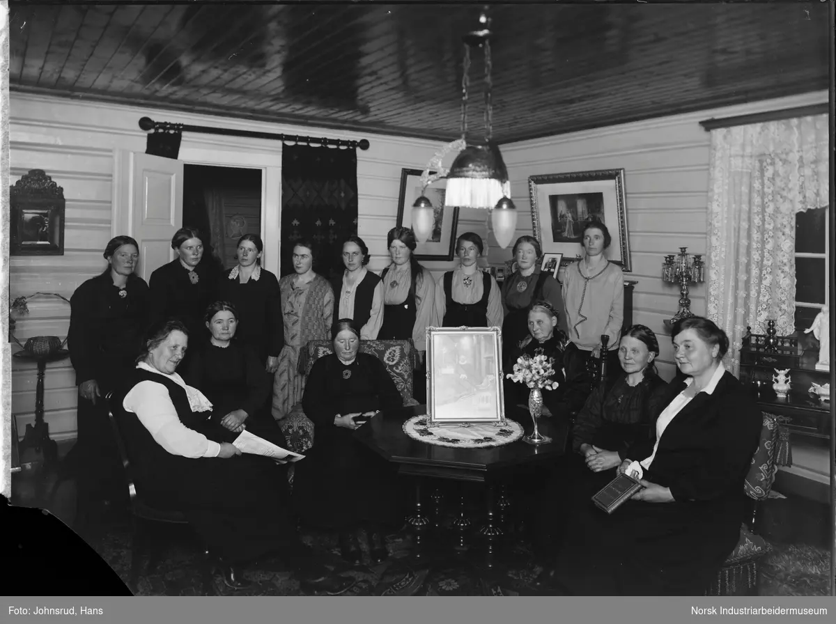 Kvinneforeningen oppstilt i stue med bilde av Sogneprest Borck på stuebordet.