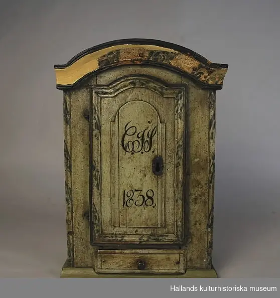 Skåp med en dörr. Inuti skåpet en hylla och nedanför dörren en låda. Skåpet är målat i blågrönt med marmorerade kanter. På skåpsdörren ett monogram "CIS 1838."