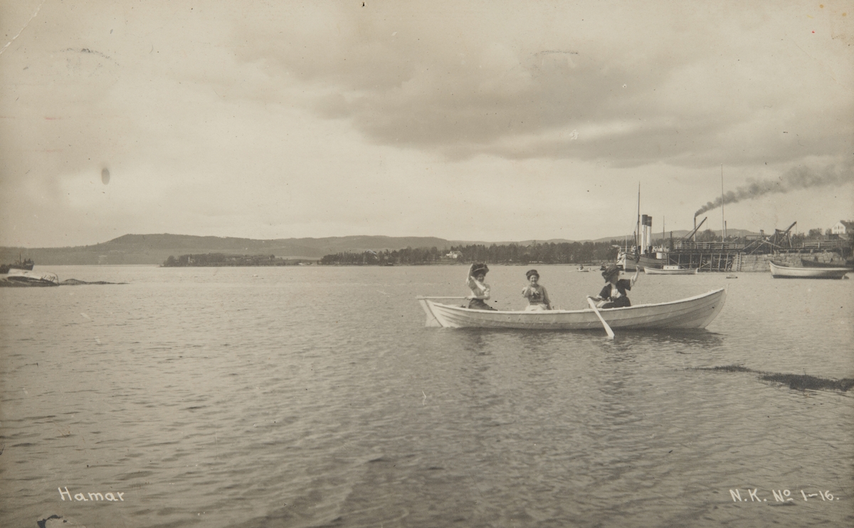 Postkort, Hamar, 3 damer ror i en robåt, i bakgrunnen D/S Kong Oscar ved Jernbanebrygga, Hamarbukta, 
