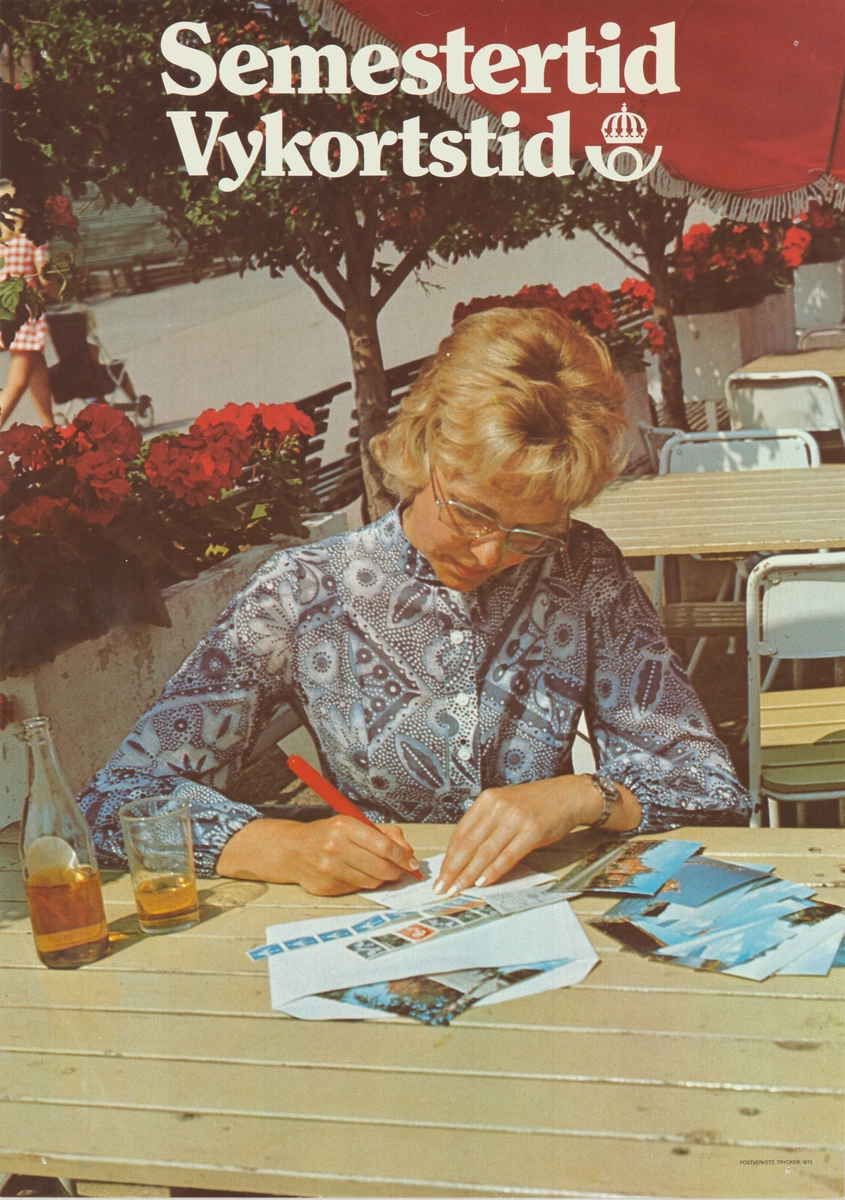 Kvinna sitter utomhus och skriver vykort. Postsymbol.