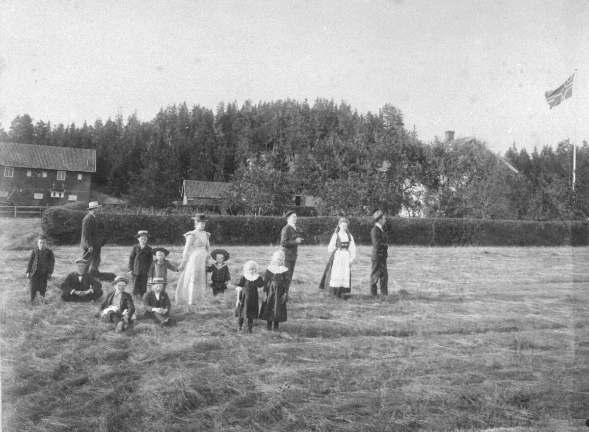 Familiebilde av familien Gjersøe, på Bakke i 1905, hage, uthus, hekk, pyntet, drakt, bunad, generasjoner, tjenestefolk, gård