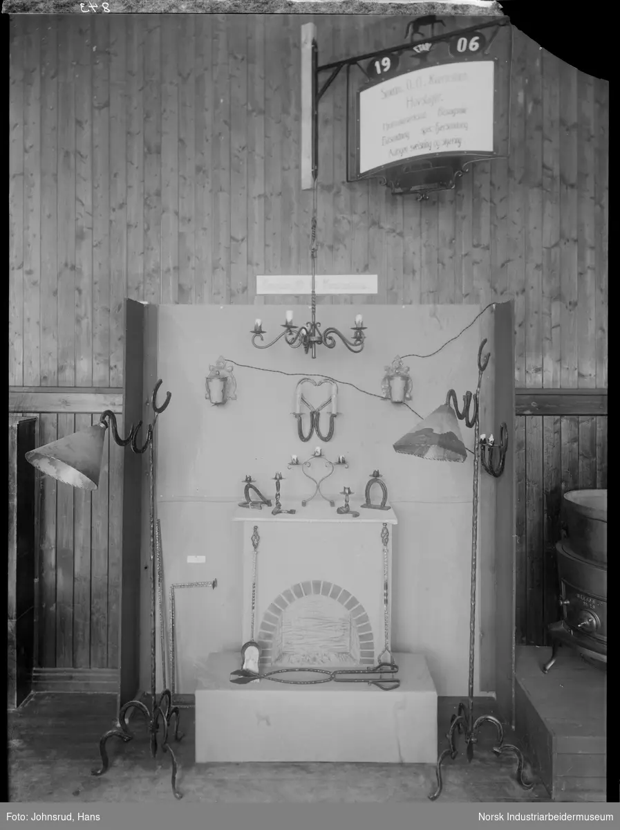 Handelsstevnet i Notodden 1933. Utstilling for hovslager og smed O. O. Kvernstein. Smidde lamper, lysestaker og ildraker stilt ut ved fiktiv peis.
