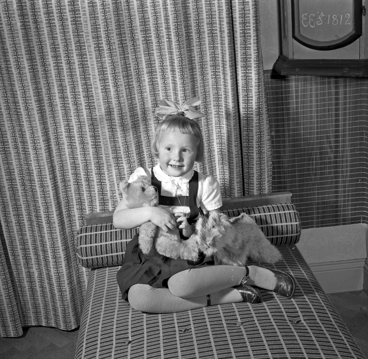 Familjen Hilda Ström, liten flicka sitter på sängen med leksaker