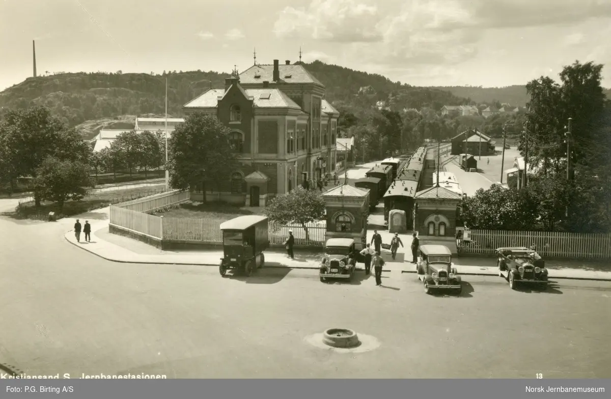 Kristiansand stasjon. Personvogner står på stasjonen. Moderne biler i forgrunnen