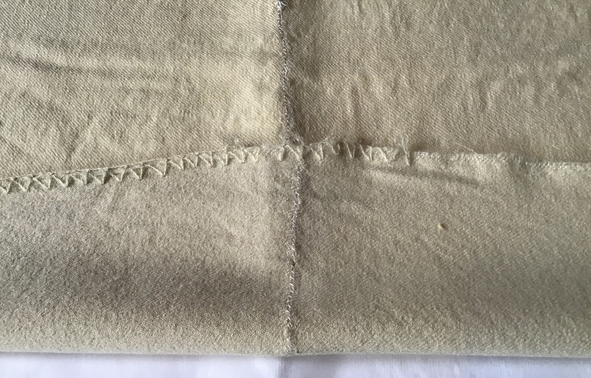 Teppe av vevd ull. Det er sydd sammen på midten av to stykker. Øverst og nederst er fem striper med blågrå garn.