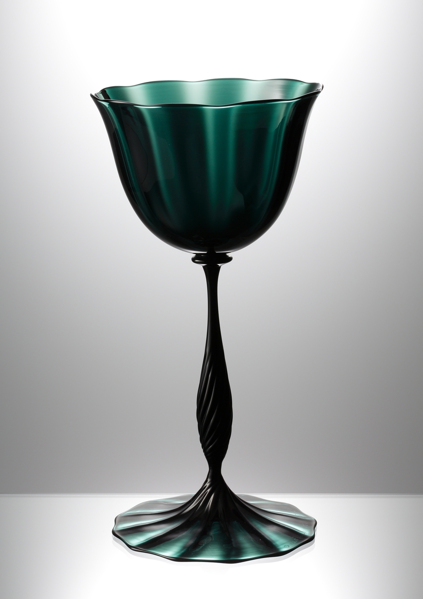 "Slottsglas" formgivet av Simon Gate till Göteborgsutställningen 1923. Friblåst och räfflat i grön glas. Fot och kupa blåsta och drivna. Räfflat balusterformat ben.
