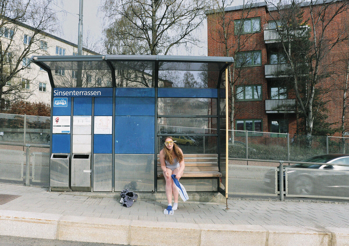 En ung kvinne sitter i et busskur i Oslo og tar på seg svømmeføtter
