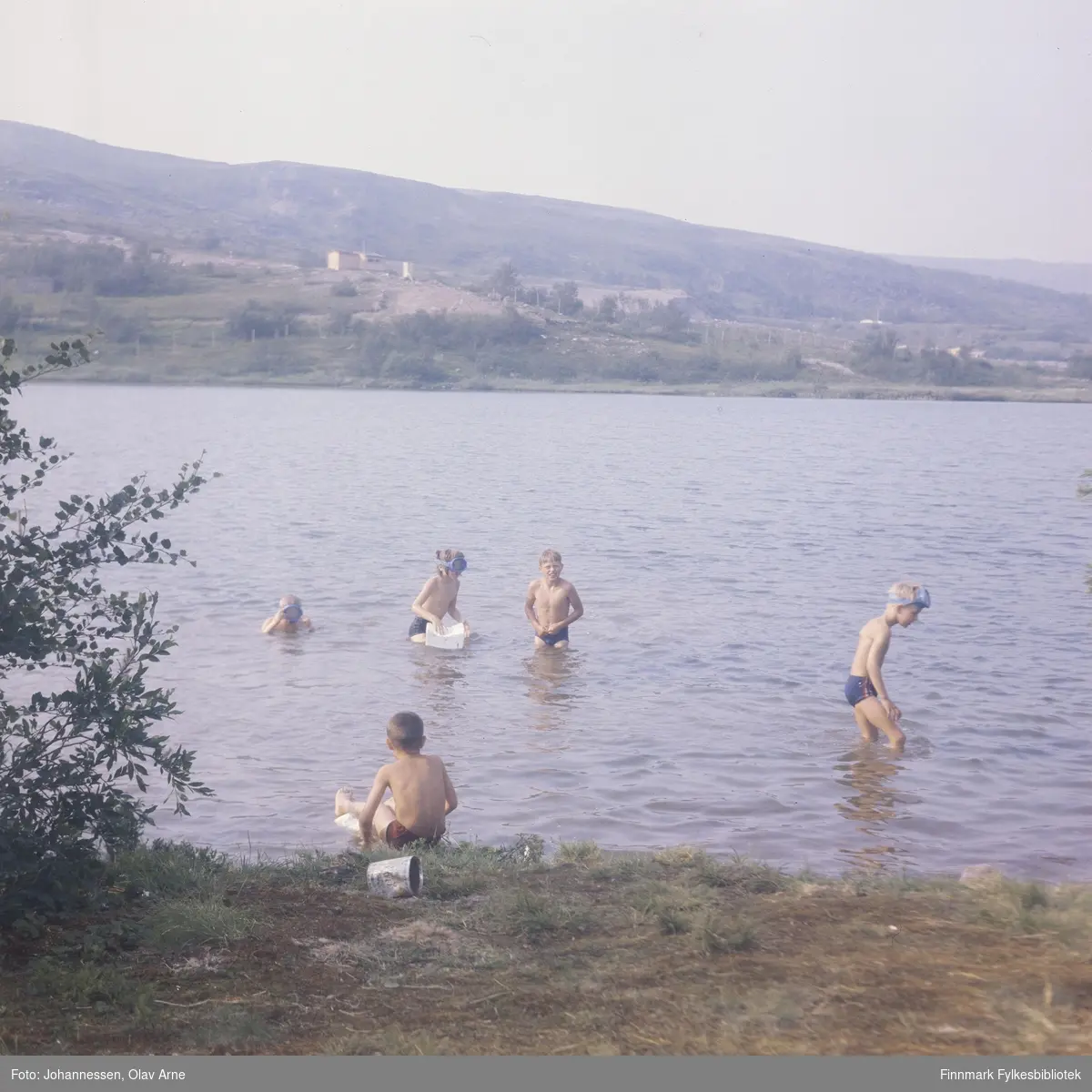 Foto av barn som bader i Båtsfjorddalen i Jovannet. Flere har på seg dykkemasker 

Gutten som er står som nummer tre fra venstre kan være John Johansen (også kalt KarlaJohn), usikker identifisering 

Foto trolig tatt på 1960/70-tallet