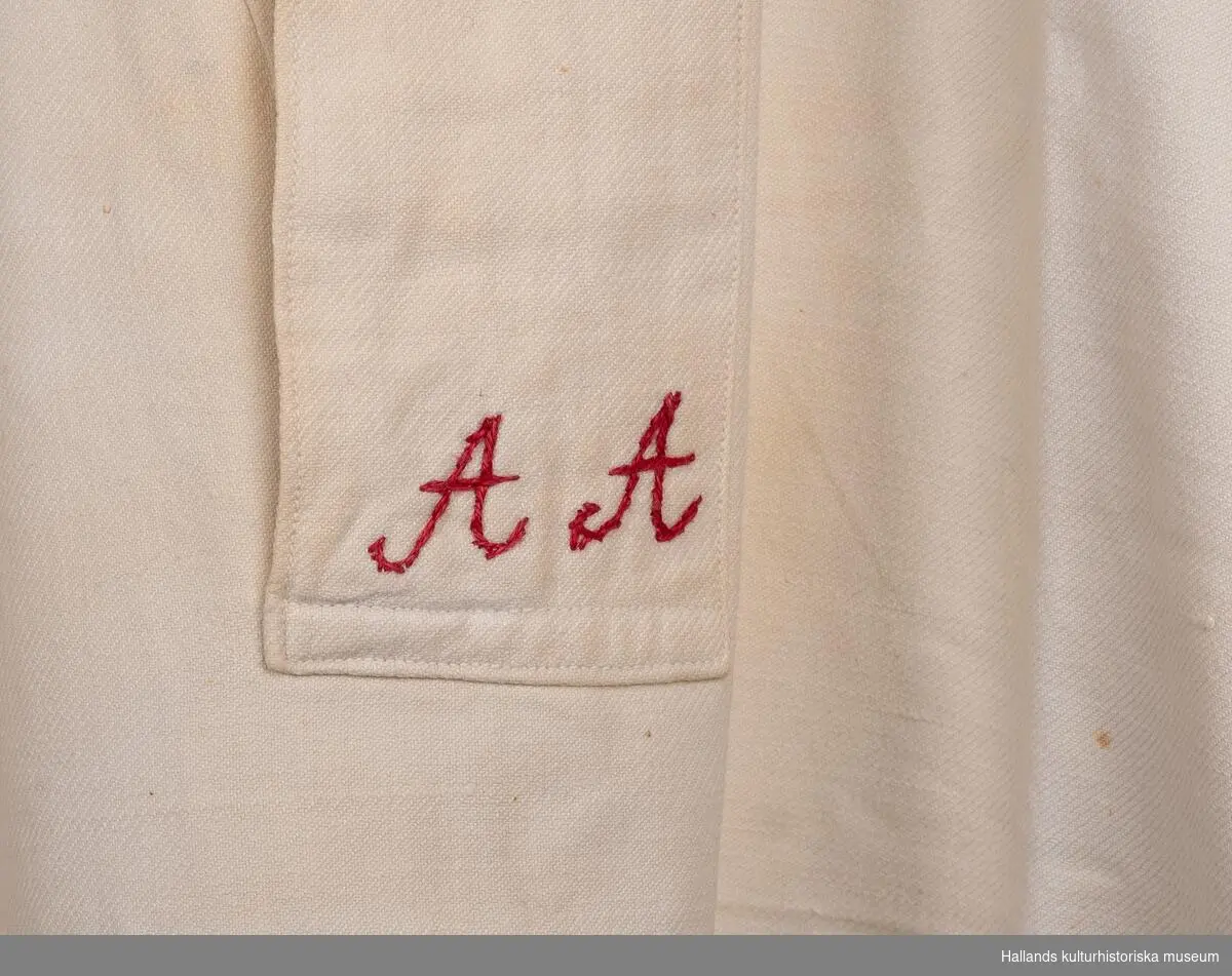 Skjorta av kypertvävd bomull, maskinvävd, lång ärm, sprund med slå framtill. Märkt "AA" med rött bomullsgarn framtill.